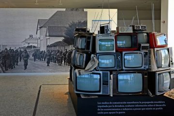 Imagen de una pirámide de televisores en el frente y por detrás un cuadro de un ejército