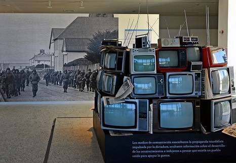 Imagen de una pirámide de televisores en el frente y por detrás un cuadro de un ejército